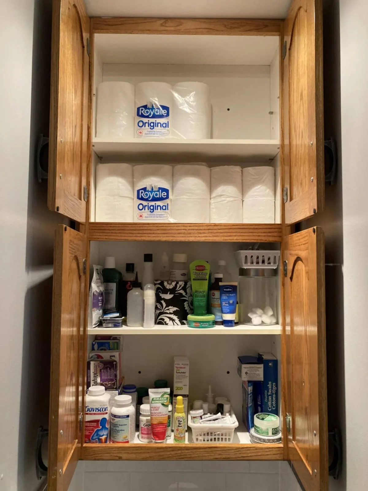 After: the same cupboard with paper rolls stacked on top and toiletries sorted into baskets below