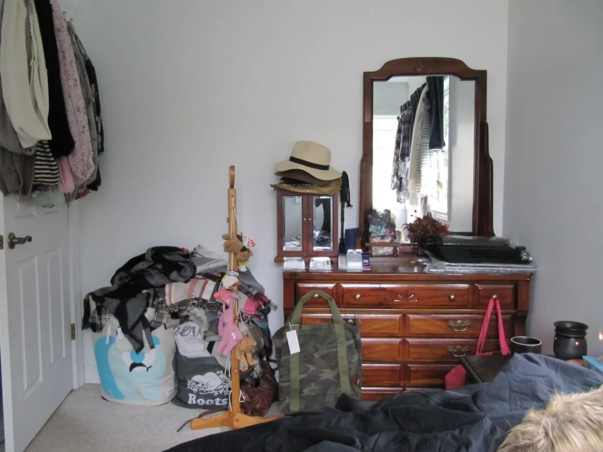Before: a bedroom with clothes and bags piled on the floor in front of a wooden dresser
